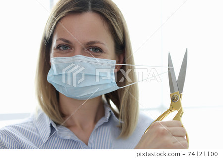 Woman cutting protective medical mask on her face with scissors 74121100