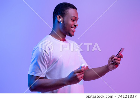 Tech Gadgets. Happy Black Guy Using Smartphone And Earpods For Listening Music 74121837