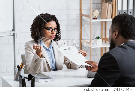 Serious personnel manager taking resume from young job applicant on work interview at modern company office Serious personnel manager taking resume from young job applicant on work interview at modern company office 74122146