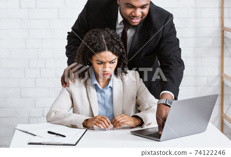 Workplace harassment. Boss touching his young attractive female assistant while she working on laptop at office 74122246
