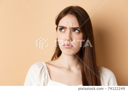Close up of angry cute girl frowning, looking aside displeased, stare at bad thing, standing on beige background 74122249