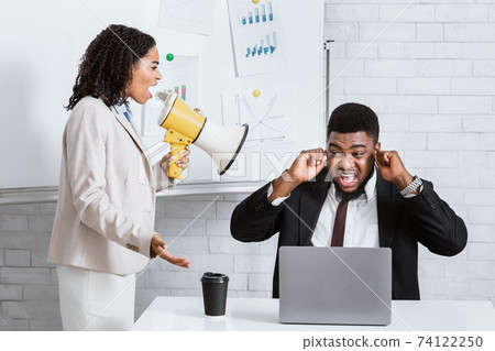 Enraged female boss with loudspeaker screaming at her scared subordinate at company office 74122250