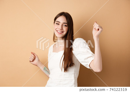 Happy woman dancing and having fun, close eyes and smiling, standing on beige background Happy woman dancing and having fun, close eyes and smiling, standing on beige background 74122319