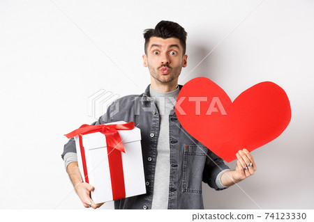 Valentines day and love concept. Guy waiting for kiss, bring lovely gifts and red heart card, pucker lips and look at camera, celebrating romantic holiday 74123330