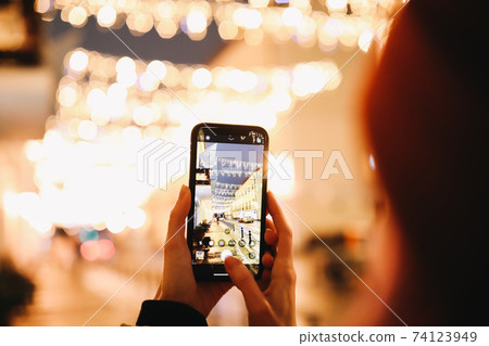 Cropped image of female photographing street on her smart phone camera. Woman taking picture of night city lights on cell telephone. Cropped image of female photographing street on her smart phone camera. Woman taking picture of night city lights on cell telephone. 74123949