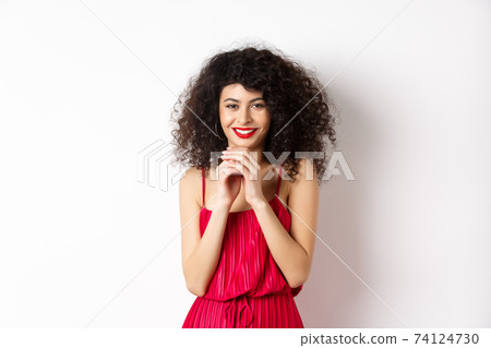 Cunning young woman with curly hair, steeple fingers and smiling devious, having a plan, standing in red dress on white background Cunning young woman with curly hair, steeple fingers and smiling devious, having a plan, standing in red dress on white background 74124730