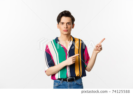 Portrait of young handsome man pointing fingers at upper right corner, showing logo, standing over white background 74125588