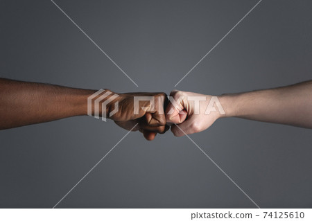 Close up of white skinned man and dark skinned man doing a fist bump. 74125610