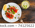 Halibut fish fillet baked with tomatoes. White plate, lemon, green basil, top view, close-up 74125622