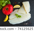 Raw halibut fish fillet, tomato, lemon basil and spices on black stone board, top view 74125625