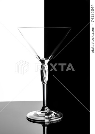 Empty transparent martini glass on mirrored surface over black and white background, studio advertising shot, copy space 74125844