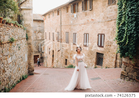 A bride in a white dress in the old town of San Gimignano.A girl walks around the city in Italy.Tuscany. 74126375