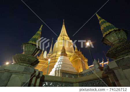 Golden pagoda at Temple of the Emerald Buddha in Bangkok, Thailand. Wat Phra Kaew and Grand palace in old town, urban city. Buddhist temple, Thai architecture. A tourist attraction at night. 74126712