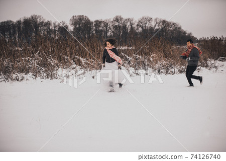 wedding couple running lying in snow laughing having fun playing snowballs wedding couple running lying in snow laughing having fun playing snowballs 74126740