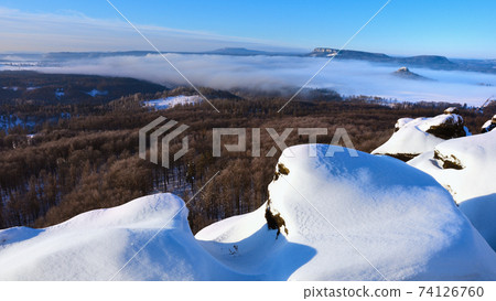 Snowy rocks above dry forests valley. Winter cold weather in mountains, colorful fog. 74126760