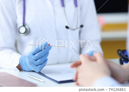 A doctor in protective gloves holds a test tube in front of a patient A doctor in protective gloves holds a test tube in front of a patient 74126861