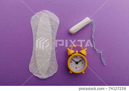 Female's menstrual cycle concept. Sanitary pad with yellow alarm clock and tampon 74127259