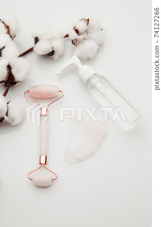 Pink Gua Sha massage tool on a table with cotton. Rose Quartz roller. Facial skin care at home, anti-aging and lifting therapy. Vertical image 74127266