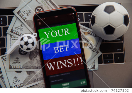 Smartphone with online gambling application, dollar bills and soccer ball on a keyboard. Betting concept Smartphone with online gambling application, dollar bills and soccer ball on a keyboard. Betting concept 74127302