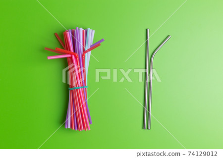Stainless steel reusable drinking straw with many multicolored plastic straws on yellow background Stainless steel reusable drinking straw with many multicolored plastic straws on yellow background 74129012