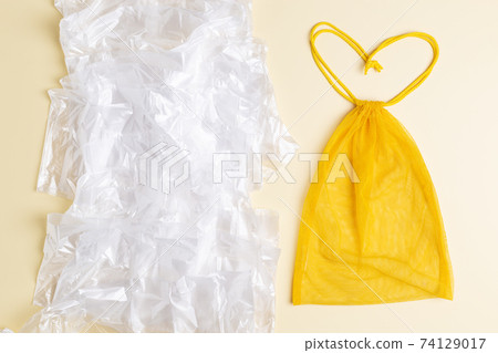 Mesh reusable yellow bag in form of heart vs a lot of plastic bags. Eco concept. Zero waste shopping Mesh reusable yellow bag in form of heart vs a lot of plastic bags. Eco concept. Zero waste shopping 74129017