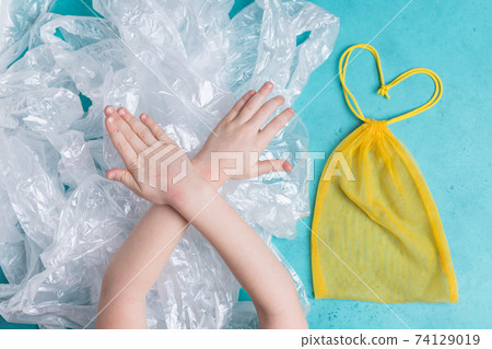 Yellow mesh reusable bag vs a lot of plastic bags little girl hands make sign to stop pollution Yellow mesh reusable bag vs a lot of plastic bags little girl hands make sign to stop pollution 74129019