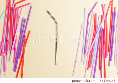 Stainless steel reusable drinking straw with many multicolored plastic straws on yellow background Stainless steel reusable drinking straw with many multicolored plastic straws on yellow background 74129021