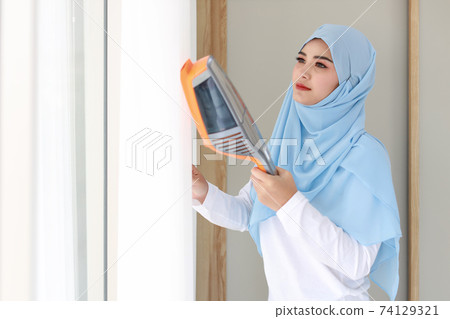 Active young beautiful asian muslim housewife woman cleaning white curtain with vacuum cleaning Cleaning girl in black leggings vacuuming her room in the morning 74129321