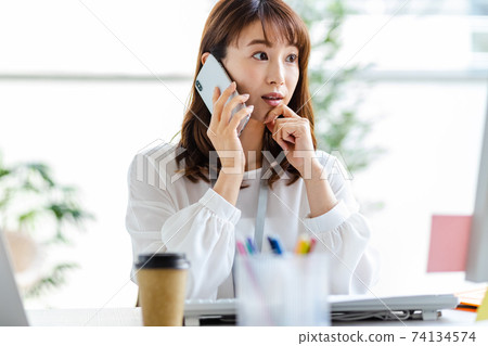 A woman talking on her smartphone during desk work 74134574