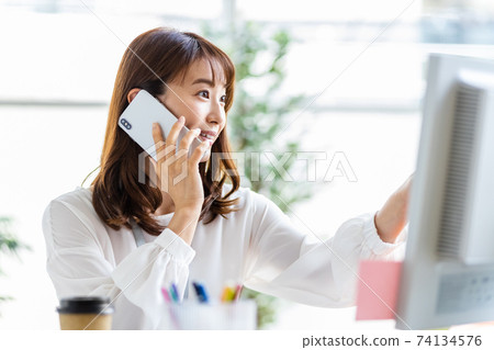 A woman talking on her smartphone during desk work 74134576