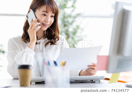 A woman talking on her smartphone during desk work 74134577