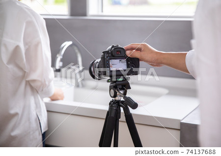 A male photographer is shooting a woman standing in the kitchen photographer A male photographer is shooting a woman standing in the kitchen photographer 74137688