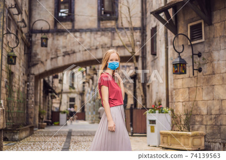 Young woman tourist wearing a medical mask during COVID-19 coronavirus walks down the street in a European city after the end of COVID-19 coronavirus. quarantine is over 74139563