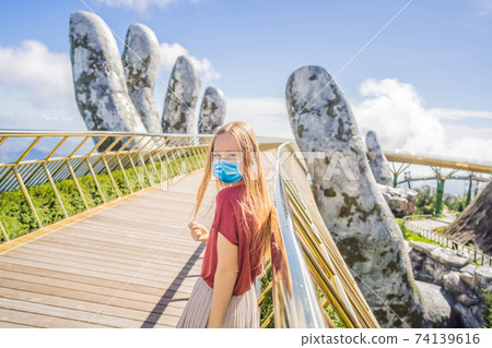 Young woman tourist wearing a medical mask during COVID-19 coronavirus at Famous tourist attraction - Golden bridge at the top of the Ba Na Hills, Vietnam 74139616