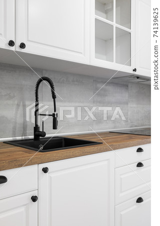 Simple and elegant kitchen with wooden countertop, white cupboards, drawers and black sink. 74139625
