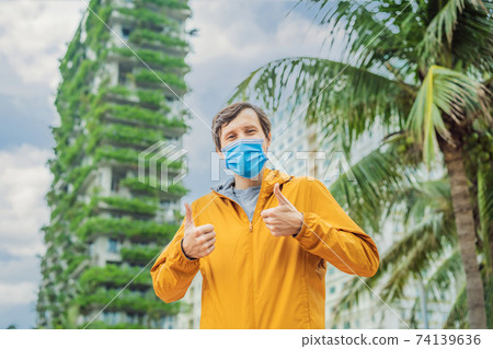 man wearing a medical mask during COVID-19 coronavirus looks at Eco architecture. Green cafe with hydroponic plants on the facade. Ecology and green living in city, urban environment concept. Modern man wearing a medical mask during COVID-19 coronavirus looks at Eco architecture. Green cafe with hydroponic plants on the facade. Ecology and green living in city, urban environment concept. Modern 74139636