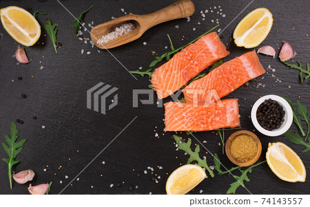 Raw fillet of salmon with sea salt, lemon and pepper on black stone background. Raw fillet of salmon with sea salt, lemon and pepper on black stone background. 74143557