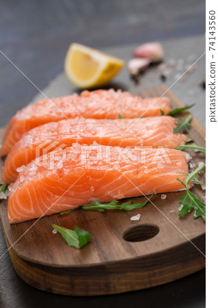 Raw fillet of salmon with sea salt, lemon and pepper on black stone background. Raw fillet of salmon with sea salt, lemon and pepper on black stone background. 74143560