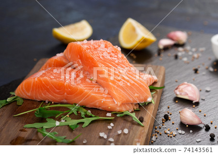 Raw fillet of salmon with sea salt, lemon and pepper on black stone background. Raw fillet of salmon with sea salt, lemon and pepper on black stone background. 74143561