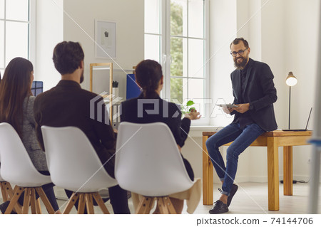 Supportive coach or team leader communicating with company employees during meeting in office 74144706