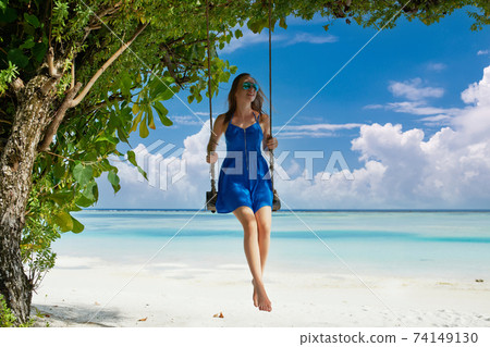 Woman in blue dress swinging at beach Woman in blue dress swinging at beach 74149130