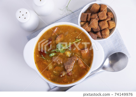 Pea soup with meat, smoked sausage, pea sprouts and croutons. Traditional Russian dish. Home kitchen. Close-up, selective focus. 74149976