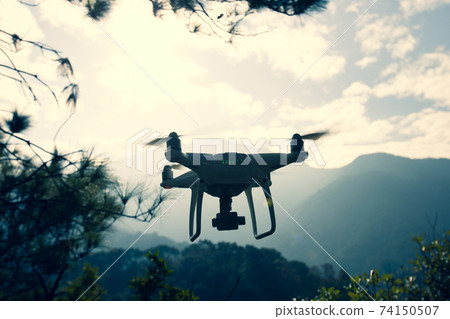 White drone with camera flying in winter tropical mountains 74150507