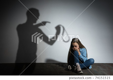 Domestic violence, abusing. Scared little caucasian girl, victim sitting close to white wall with shadow of angry father's threatening on it. Domestic violence, abusing. Scared little caucasian girl, victim sitting close to white wall with shadow of angry father's threatening on it. 74151515
