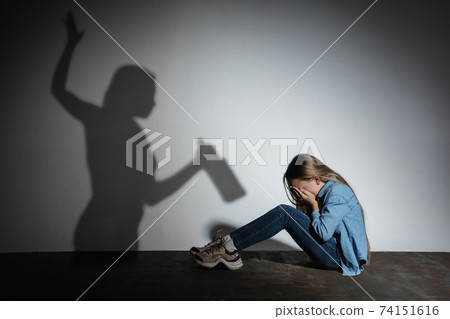 Domestic violence, abusing. Scared little caucasian girl, victim sitting close to white wall with shadow of angry threatening mother with alcohol addiction. Domestic violence, abusing. Scared little caucasian girl, victim sitting close to white wall with shadow of angry threatening mother with alcohol addiction. 74151616
