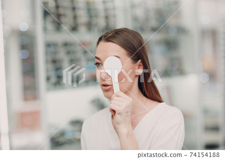 Portrait of happy young woman during eye exam at optometrist optician 74154188