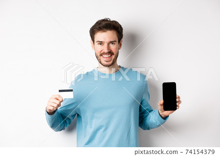 Smiling caucasian man showing plastic credit card with mobile phone screen. Guy recommending online banking app, standing on white background Smiling caucasian man showing plastic credit card with mobile phone screen. Guy recommending online banking app, standing on white background 74154379