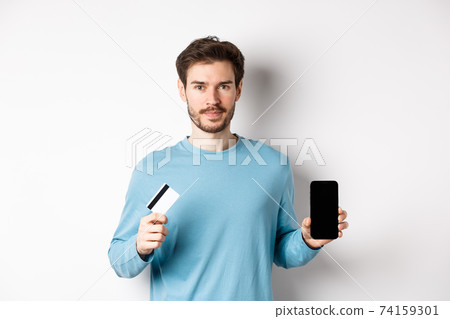 Handsome caucasian man showing empty smartphone screen and plastic credit card, standing over white background Handsome caucasian man showing empty smartphone screen and plastic credit card, standing over white background 74159301