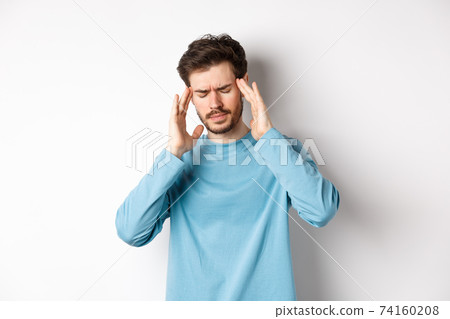 Young man having headache or hangover, touching head temples and frowning, feeling sick from migraine, standing over white background Young man having headache or hangover, touching head temples and frowning, feeling sick from migraine, standing over white background 74160208