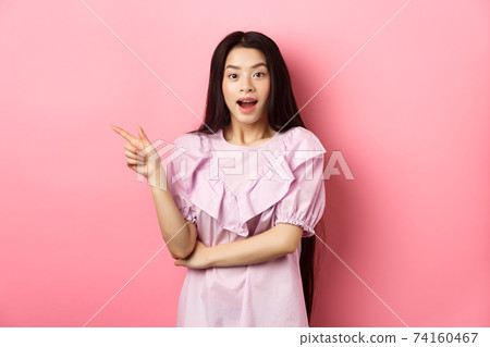 Excited beautiful asian teen girl pointing finger left, open mouth amazed and looking at camera, showing cool promo deal, pink background Excited beautiful asian teen girl pointing finger left, open mouth amazed and looking at camera, showing cool promo deal, pink background 74160467